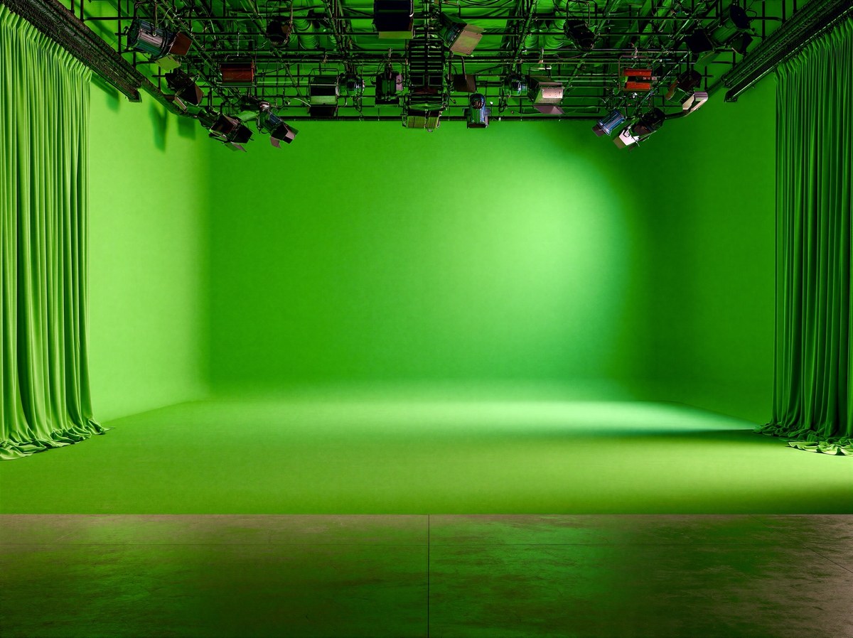 Bright green screen filming studio with green curtains, overhead lights, and an empty stage